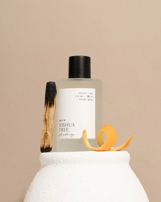 Orchid & Ash Joshua Tree room spray bottle displayed on a clay vase with burnt palo santo and orange peel.
