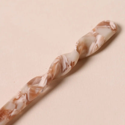 Close-up of the twisted details of the nougat colored Peignée Paris hair stick pin on neutral background.