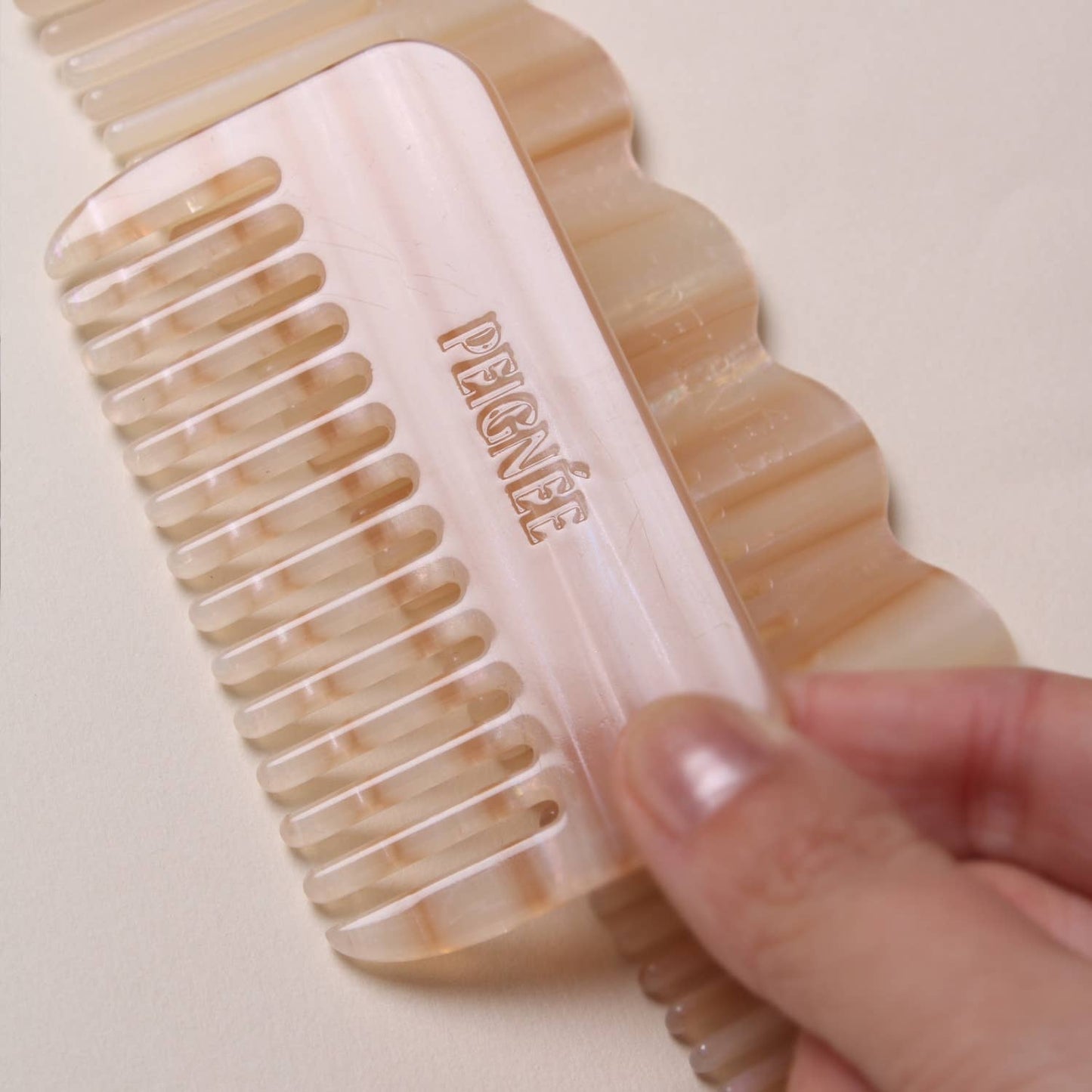 Close-up of hand holding the Peignée Paris travel comb in Latte, logo facing up.