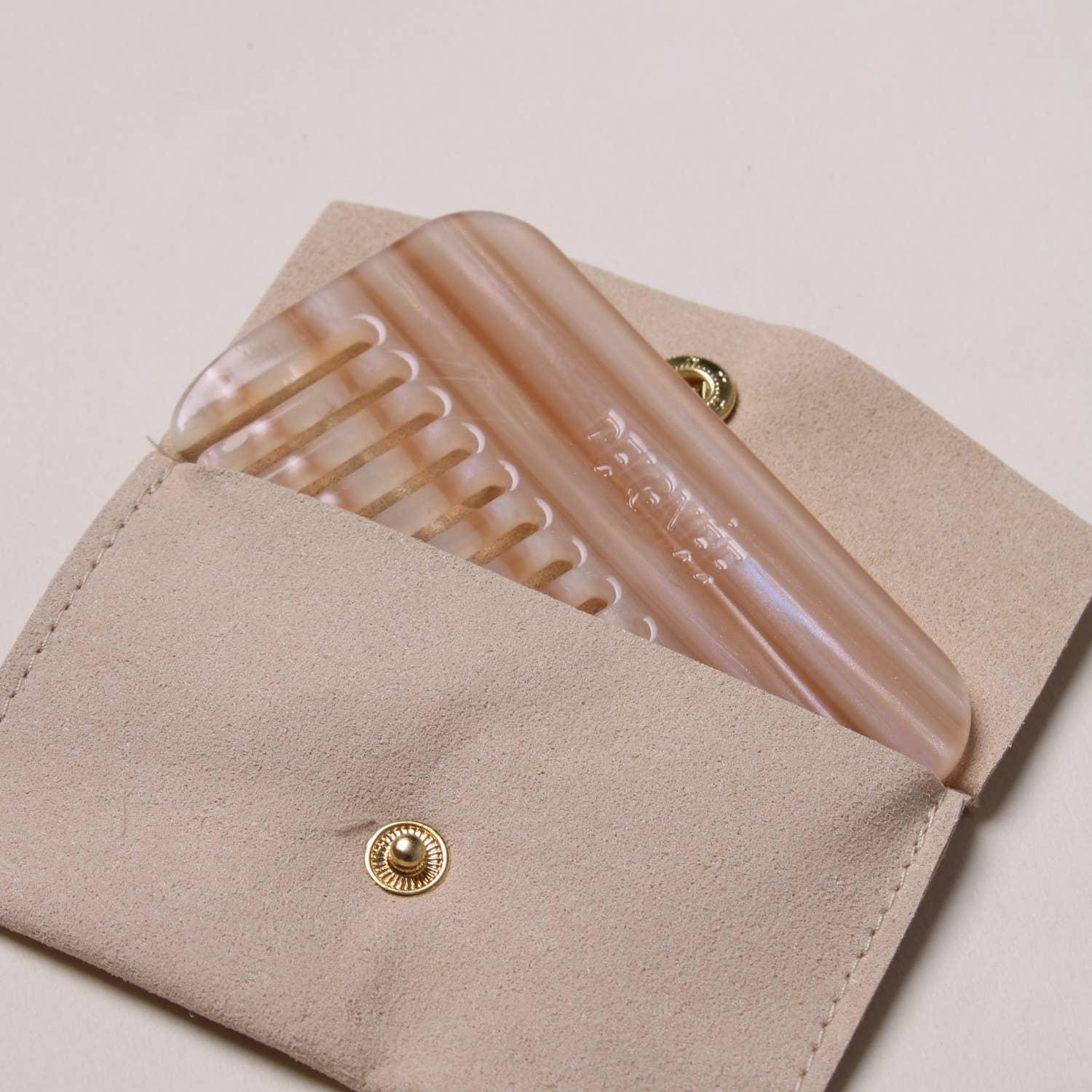 Peignée Paris Latte travel comb partially tucked inside its beige suede pouch.