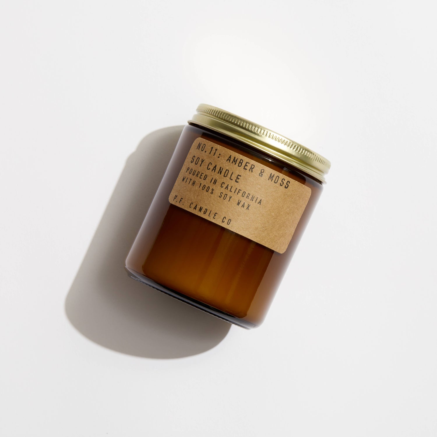 P.F. Candle Co. Amber & Moss Soy Candle resting on white surface with soft natural shadows.