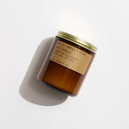 P.F. Candle Co. Amber & Moss Soy Candle resting on white surface with soft natural shadows.