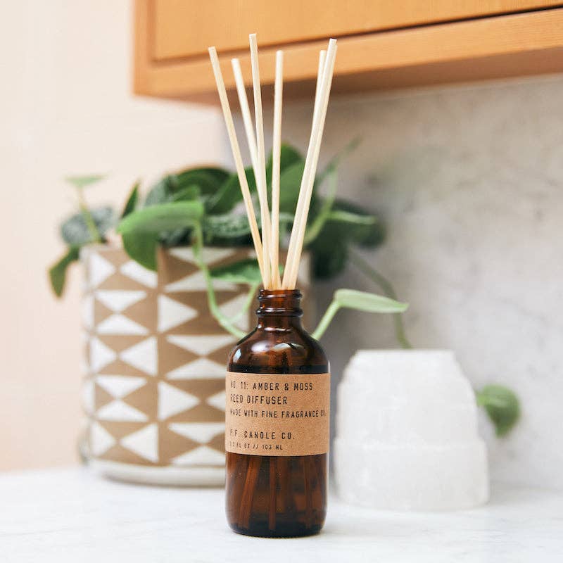 P.F. Candle Co. Amber & Moss reed diffuser styled on a bathroom counter with a geometric planter and selenite crystal.