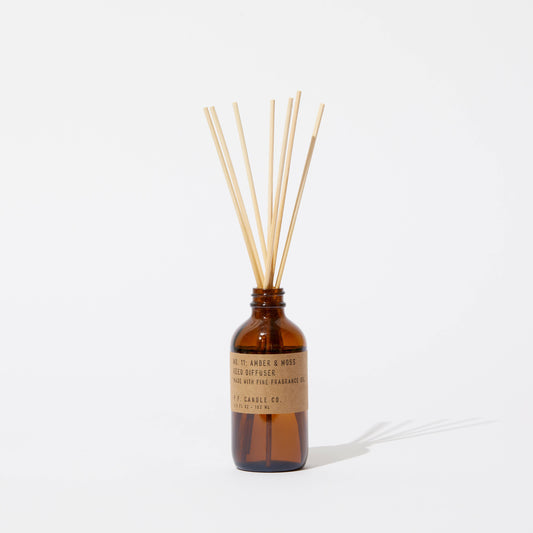 P.F. Candle Co. Amber & Moss reed diffuser bottle with sticks on white background.