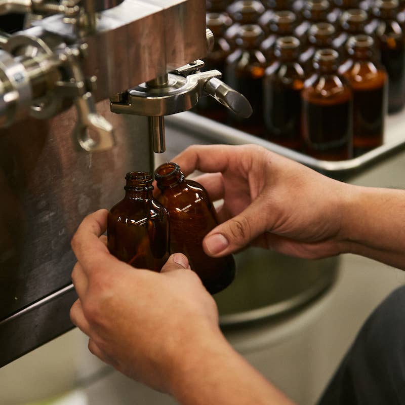 Close-up of diffuser oil being filled into amber bottles in the P.F. Candle Co. factory.