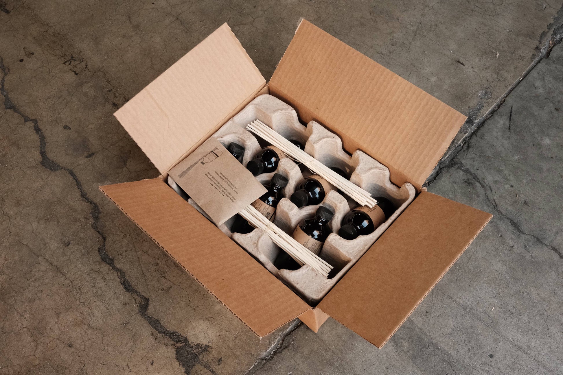 Open shipping case of P.F. Candle Co. reed diffusers showing amber bottles, reeds, and protective trays inside.