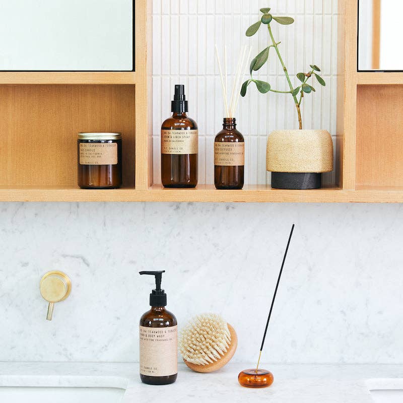 Full Teakwood & Tobacco product lineup displayed on wooden bathroom shelves with greenery.