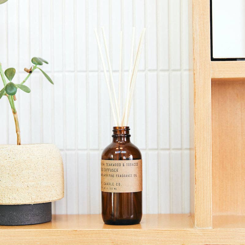 Reed diffuser by P.F. Candle Co. styled on a wood shelf next to a minimalist planter.