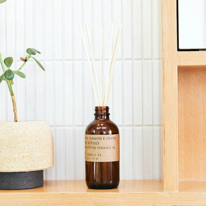 Reed diffuser by P.F. Candle Co. styled on a wood shelf next to a minimalist planter.