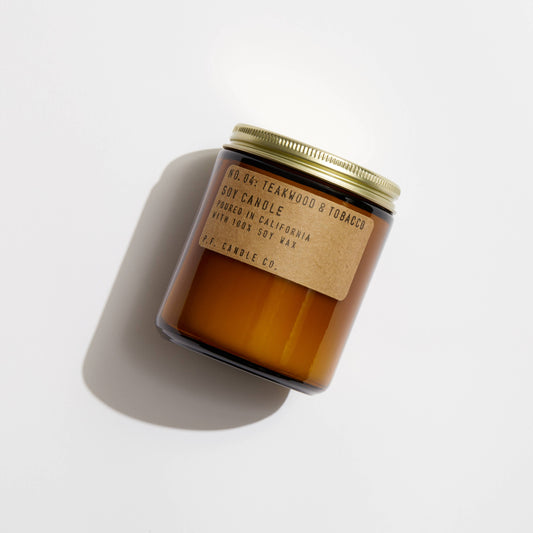 Teakwood & Tobacco soy candle by P.F. Candle Co. laying on white background, casting soft shadow.