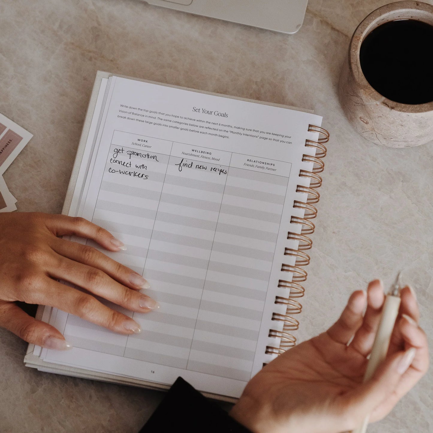 Close-up of hands filling in goal setting intentions in The Self Care Planner, setting personal work, wellbeing and relationship goals.