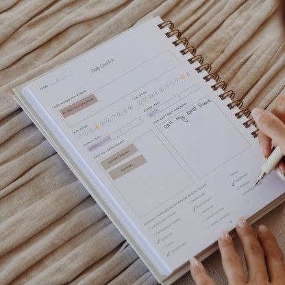 Close-up of The Inner Work Journal open to the daily check-in page, with a hand filling out entries using stickers and notes.