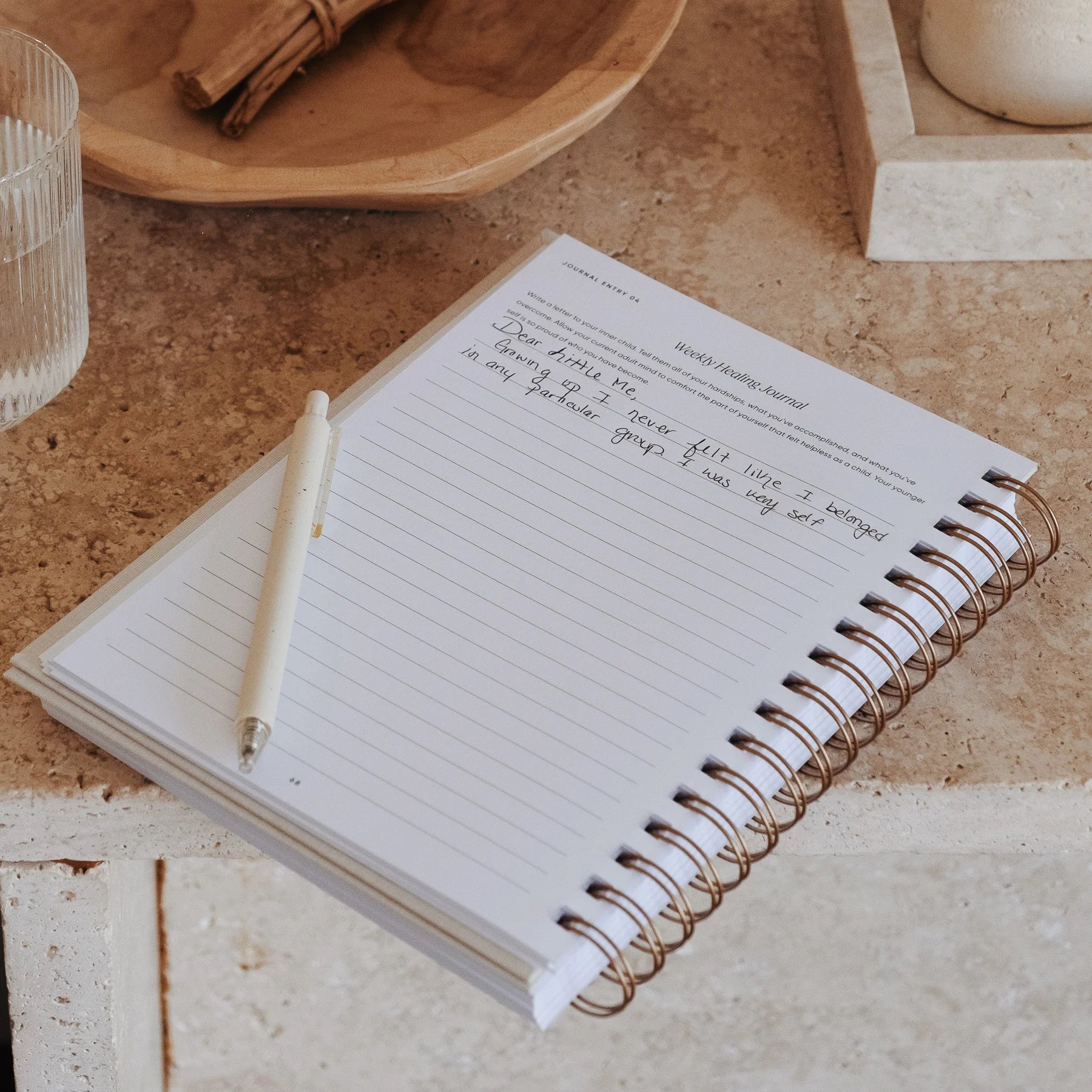 The Inner Work Journal open to a weekly healing journal page with notes on a stone table with a pen resting on the page.