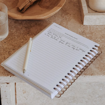 The Inner Work Journal open to a weekly healing journal page with notes on a stone table with a pen resting on the page.