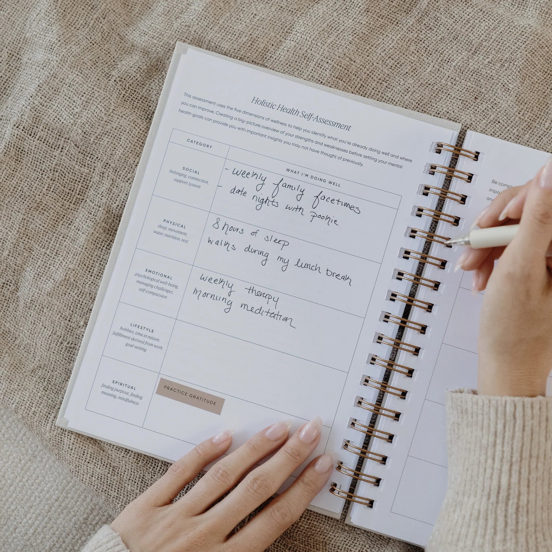 Hands holding a pen while writing in the holistic health self-assessment section of The Inner Work Journal.