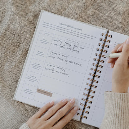 Hands holding a pen while writing in the holistic health self-assessment section of The Inner Work Journal.