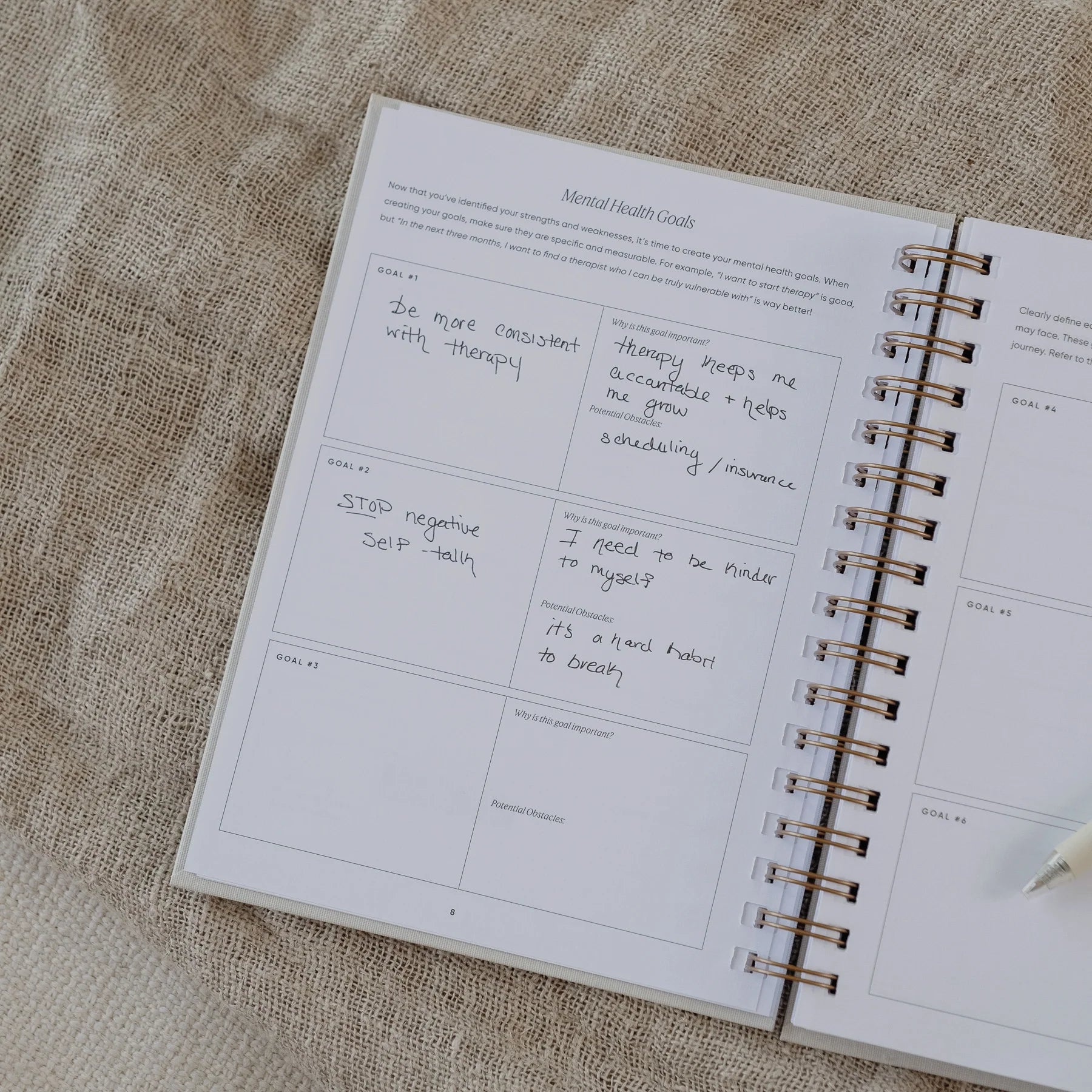 The Inner Work Journal open to the mental health goals page with handwritten entries and a pen resting beside.