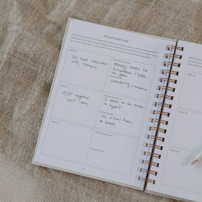 The Inner Work Journal open to the mental health goals page with handwritten entries and a pen resting beside.