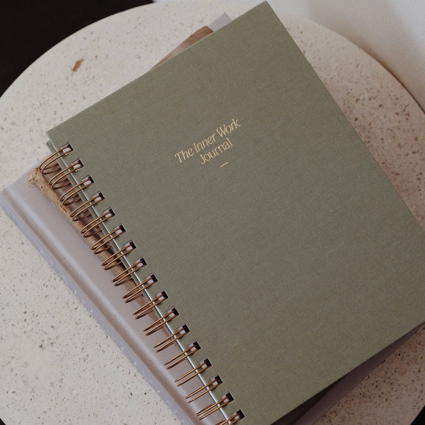 The Inner Work Journal in sage green color resting on a tabletop, paired with a neutral-toned setting for a calming aesthetic.