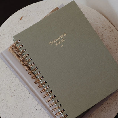 The Inner Work Journal in sage green color resting on a tabletop, paired with a neutral-toned setting for a calming aesthetic.