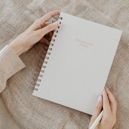 Hands gently holding The Inner Work Journal in sand, placed on a linen fabric surface.
