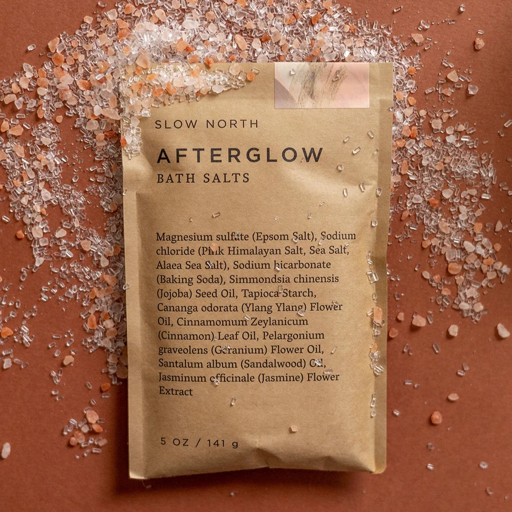 Slow North Afterglow Bath Salts flat lay with pink salt crystals scattered on a warm brown surface.