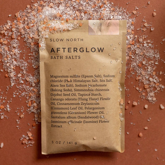 Slow North Afterglow Bath Salts flat lay with pink salt crystals scattered on a warm brown surface.