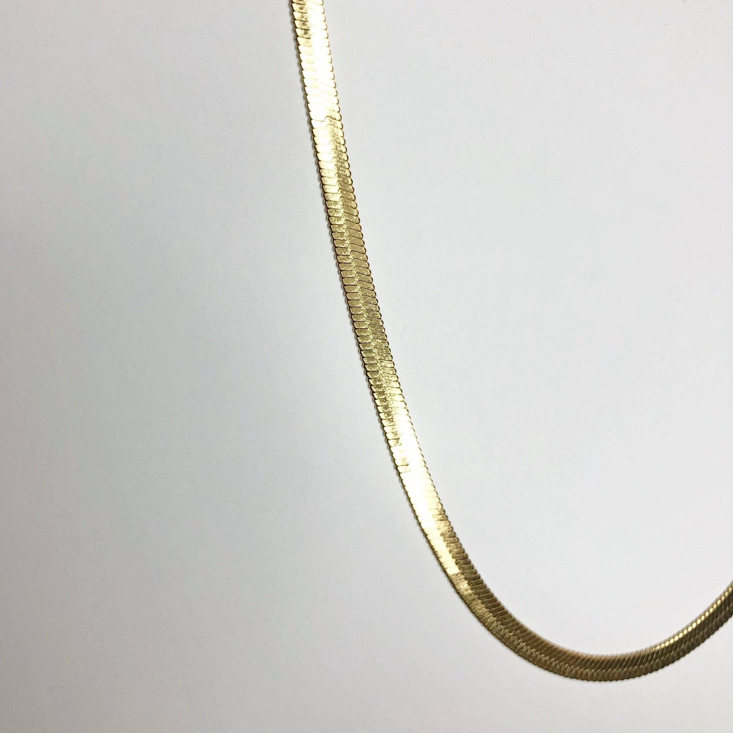 Zoomed-in detail of gold herringbone texture on chain necklace.
