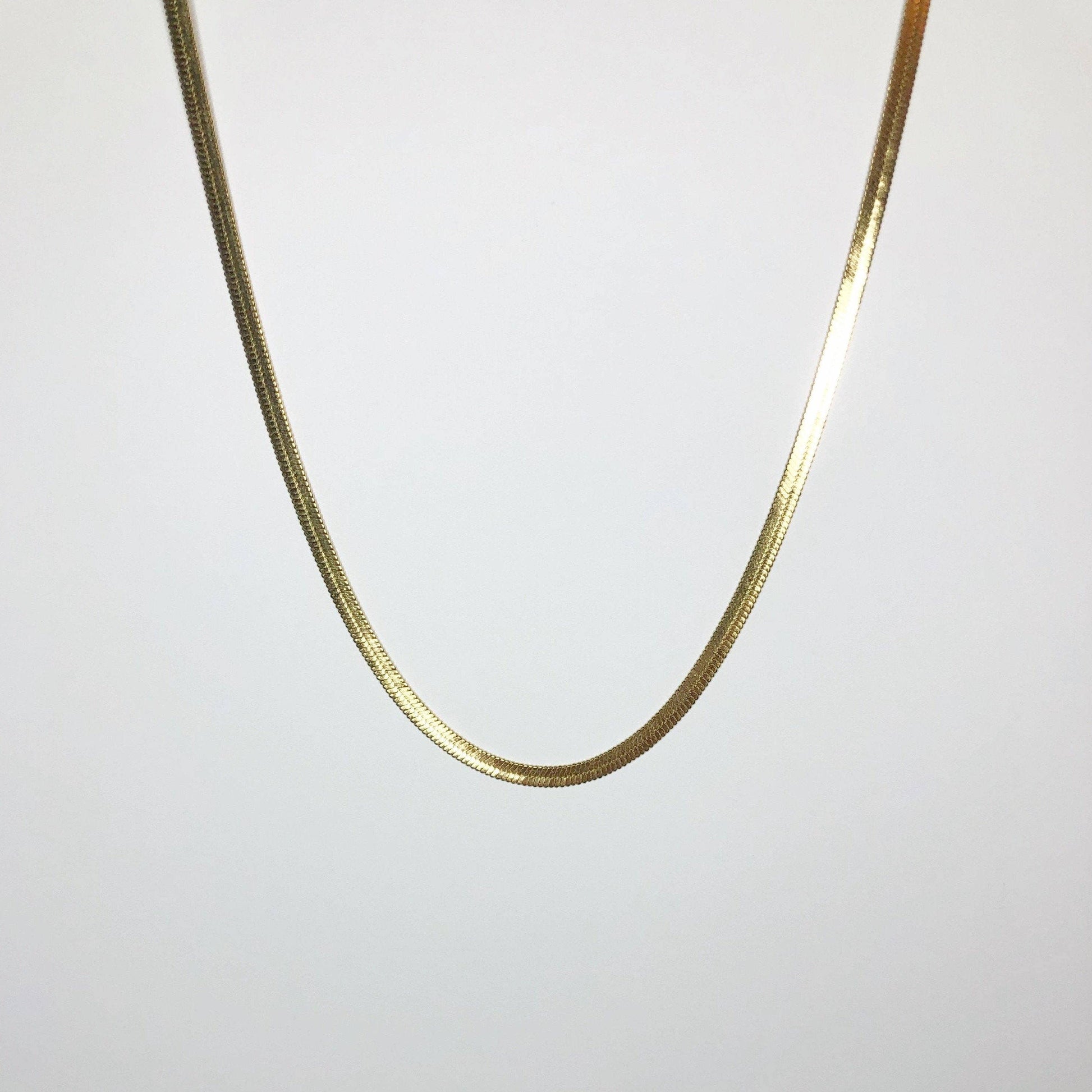 Full-length view of gold snake herringbone chain necklace hanging against white background.