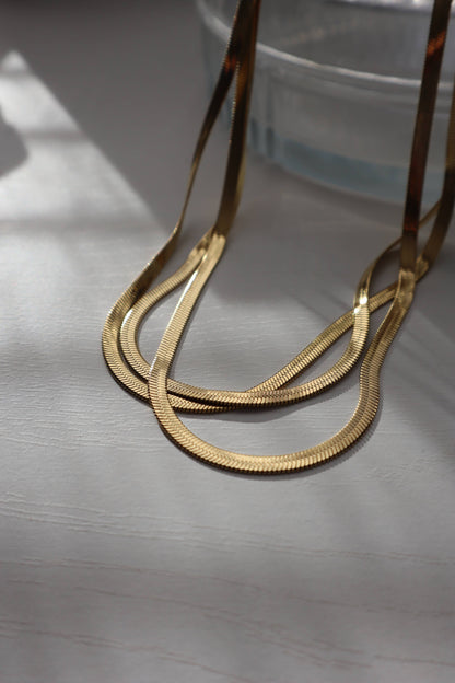  Gold snake chain necklace draped in soft daylight showing texture across white grey table.