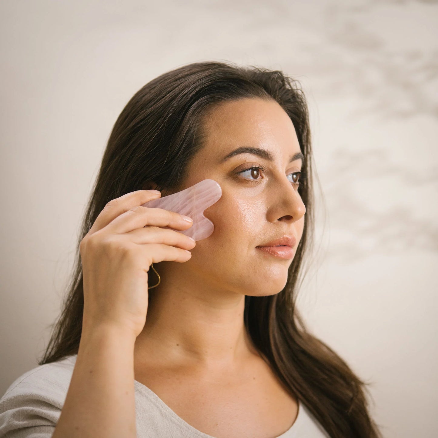 Woman demonstrating how to use the Rose Quartz Gua Sha tool on the upper cheek area.