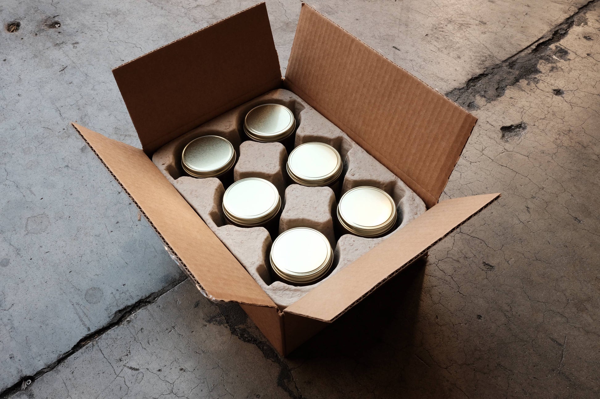 Overhead view of P.F. Candle amber jar candles with gold lids packed in a shipping box with kraft dividers.