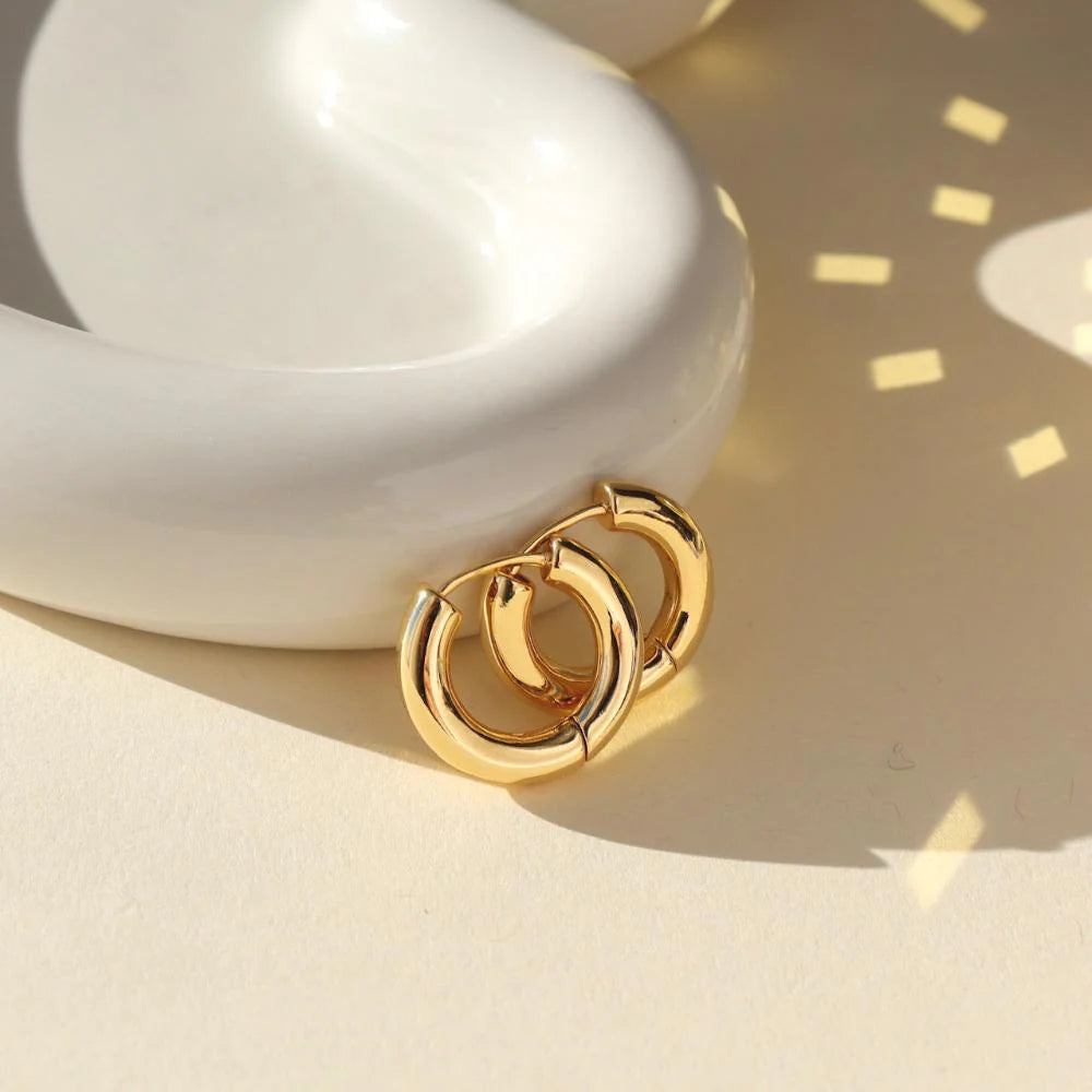 Token Jewelry Everyday Hoops gold earrings resting on side of a white ceramic dish with sunlight reflections.