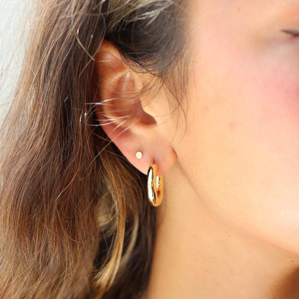 Model wearing Token Jewelry Everyday Hoops gold earrings, close-up of ear for scale.