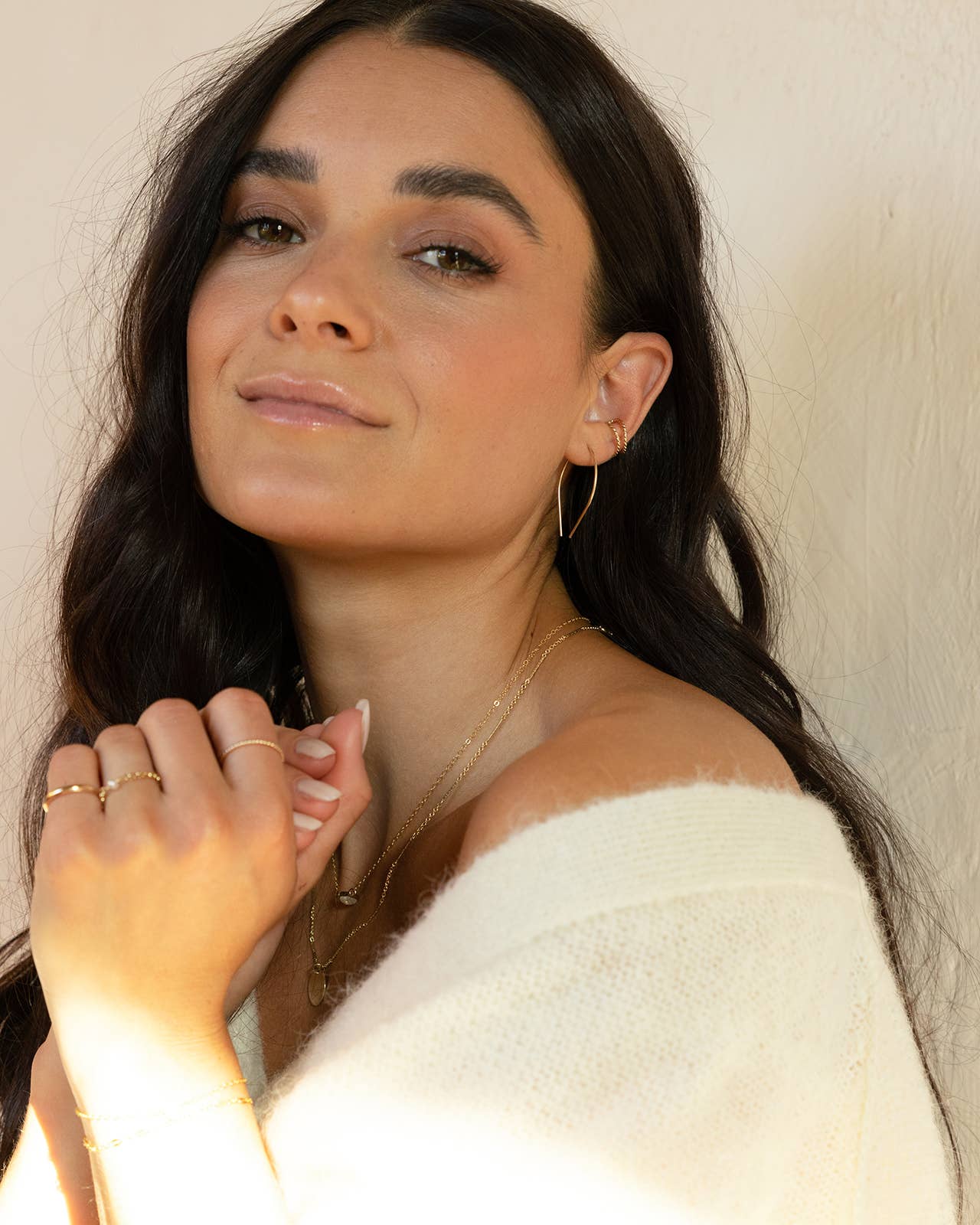 Model wearing Token Jewelry Horseshoe Earrings in gold with layered necklaces and cozy sweater.