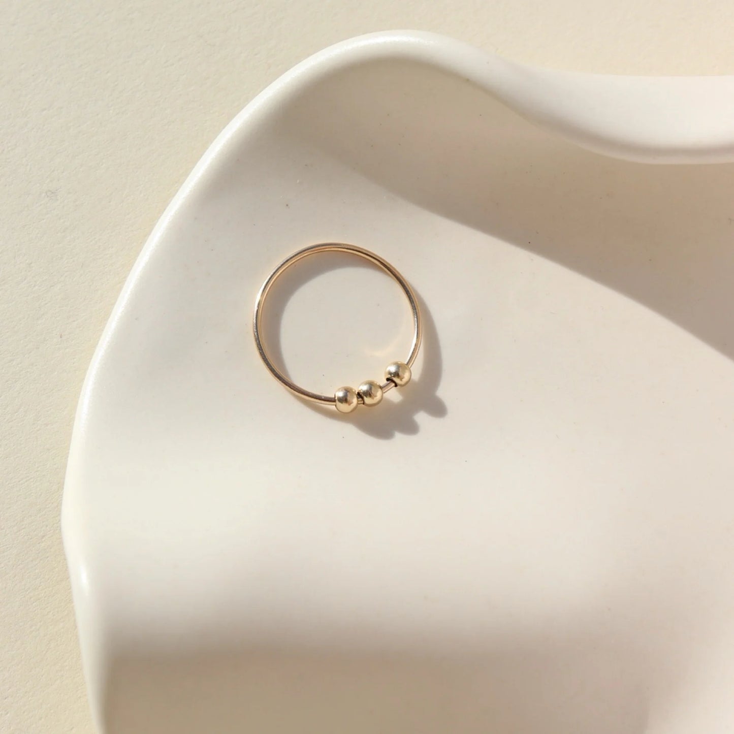 Token Jewelry Meridian Fidget Ring in gold displayed flat in a sculpted ceramic dish with soft light.