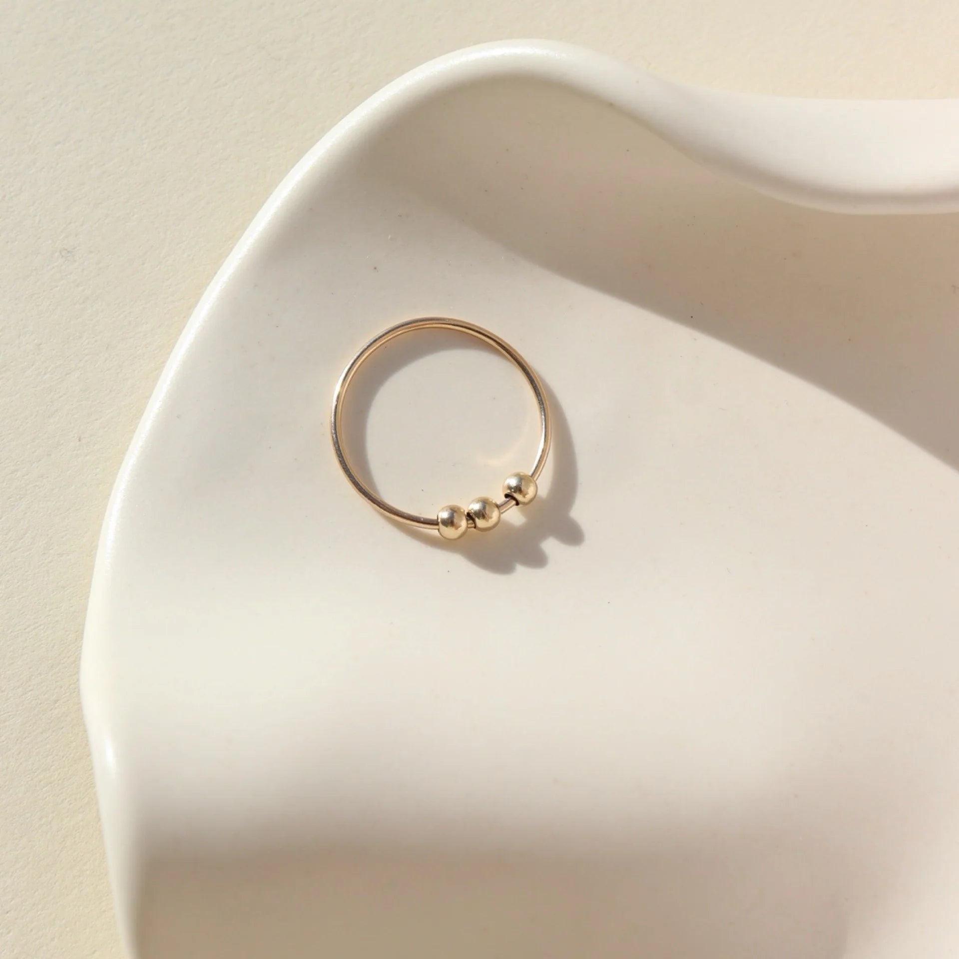 Token Jewelry Meridian Fidget Ring in gold displayed flat in a sculpted ceramic dish with soft light.