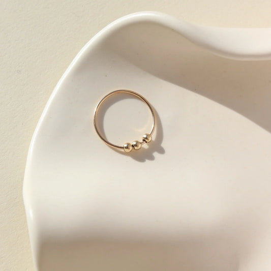 Token Jewelry Meridian Fidget Ring in gold displayed flat in a sculpted ceramic dish with soft light.