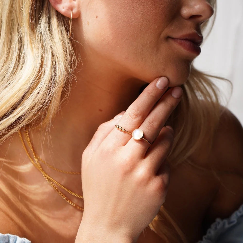 Model wearing Token Jewelry Meridian Fidget Ring in gold, styled with layered necklaces.