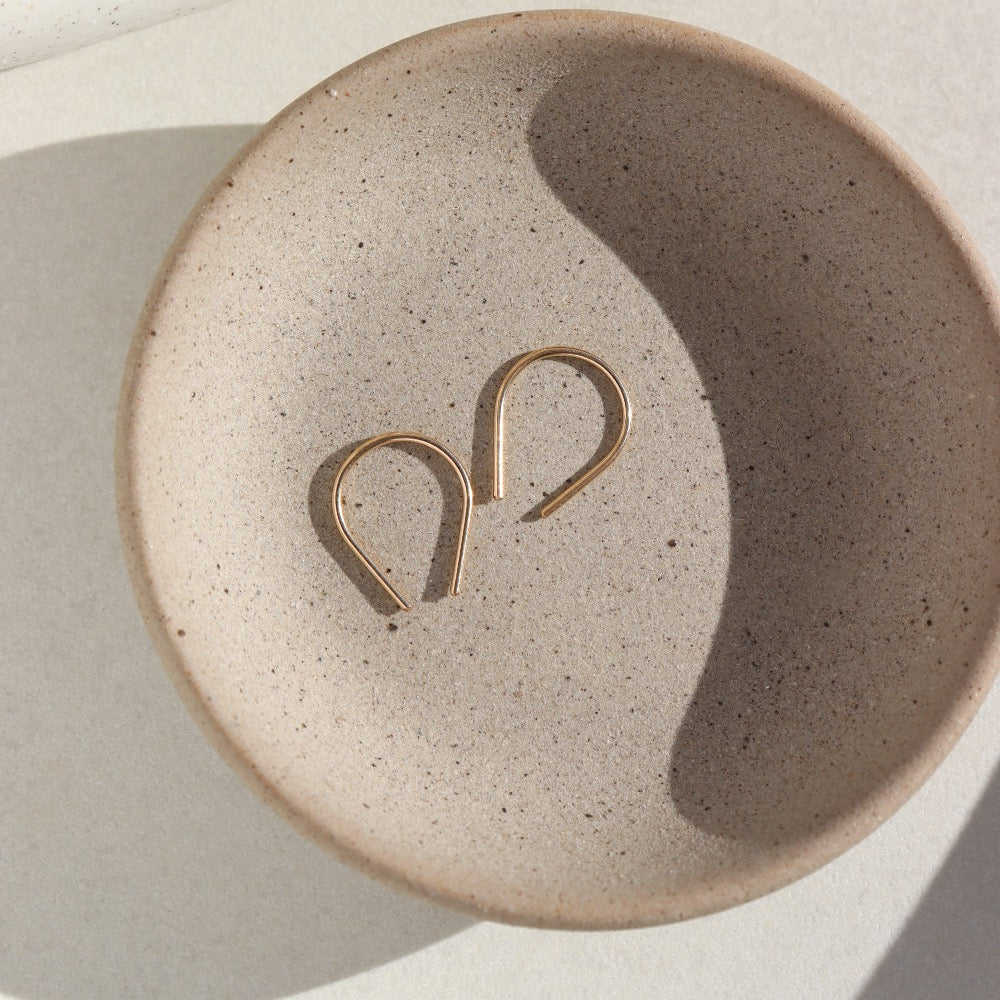 Pair of Token Jewelry Mini Horseshoe Earrings in gold resting in a ceramic dish, angled overhead shot.