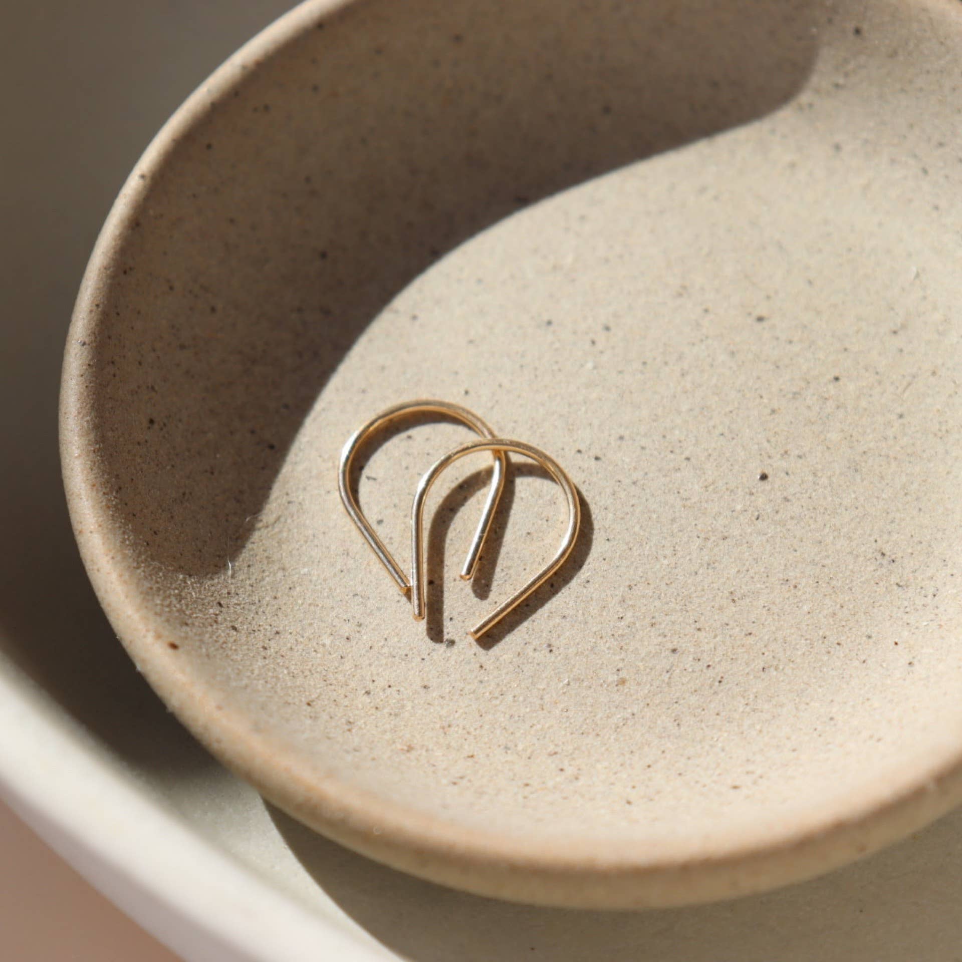 Token Jewelry Mini Horseshoe Earrings in gold displayed side by side in a neutral-toned ceramic bowl.