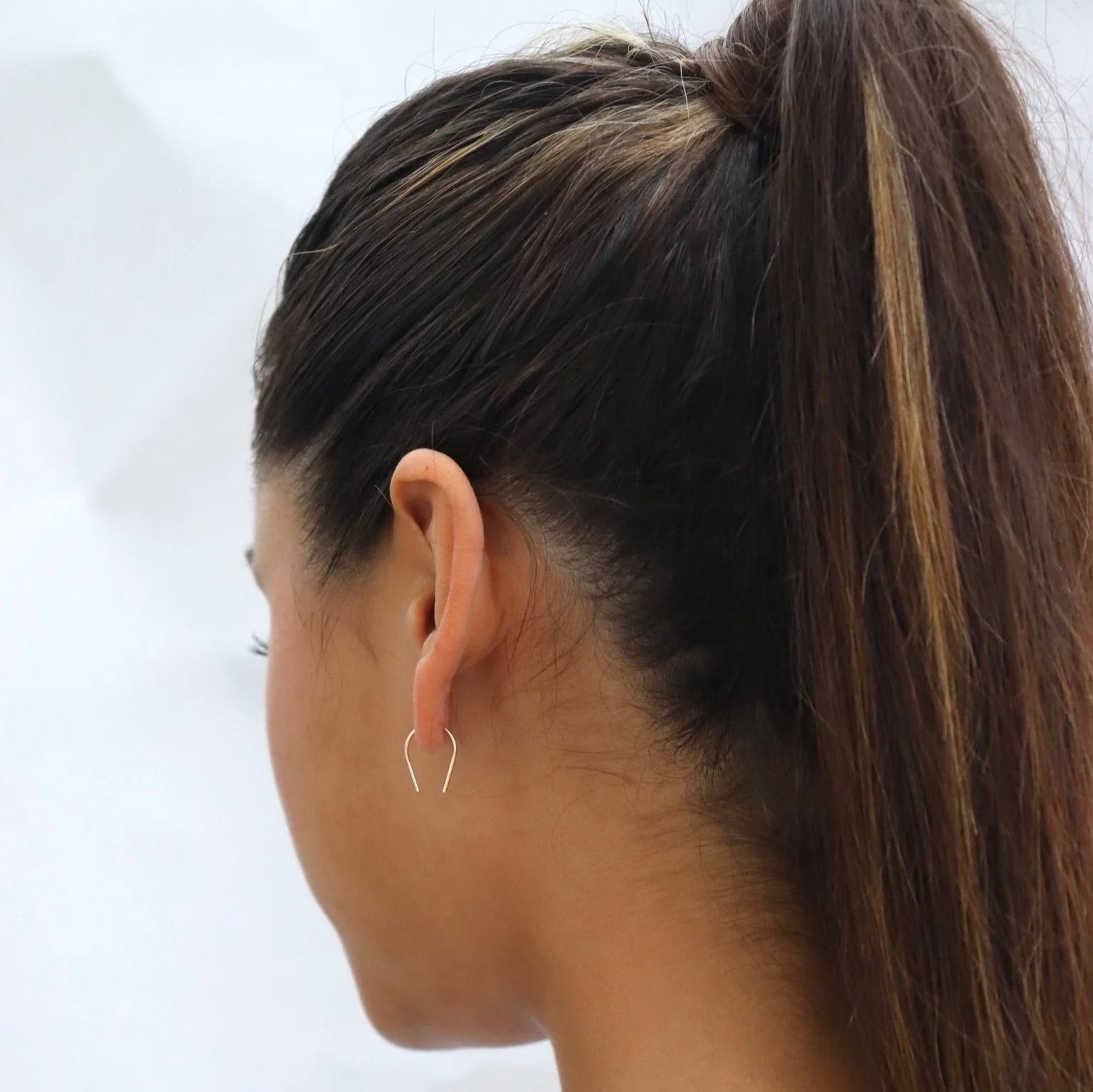 Woman wearing Token Jewelry Mini Horseshoe Earrings in gold with long brunette hair in a high ponytail.