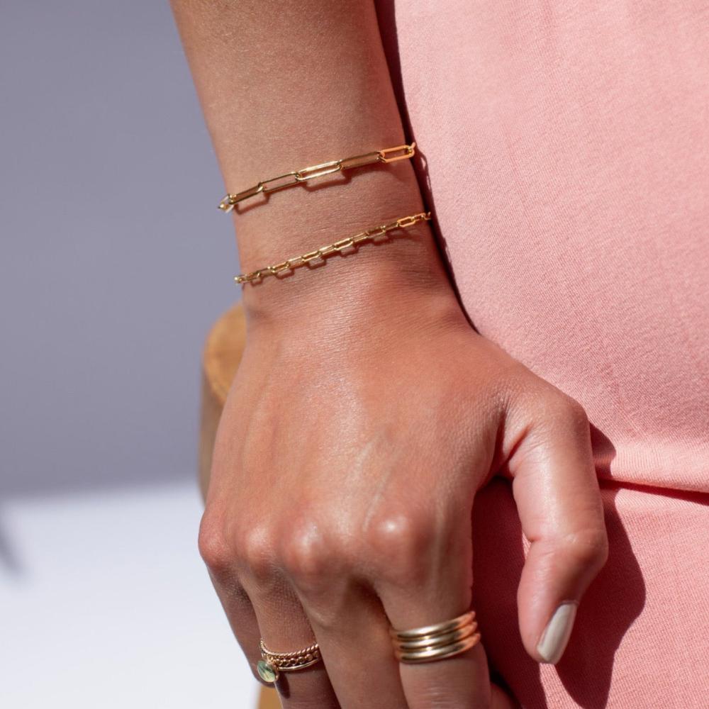 Gold Token Jewelry Narrow Links Bracelet worn with another bracelet and stacked rings, closeup of hands and wrist.