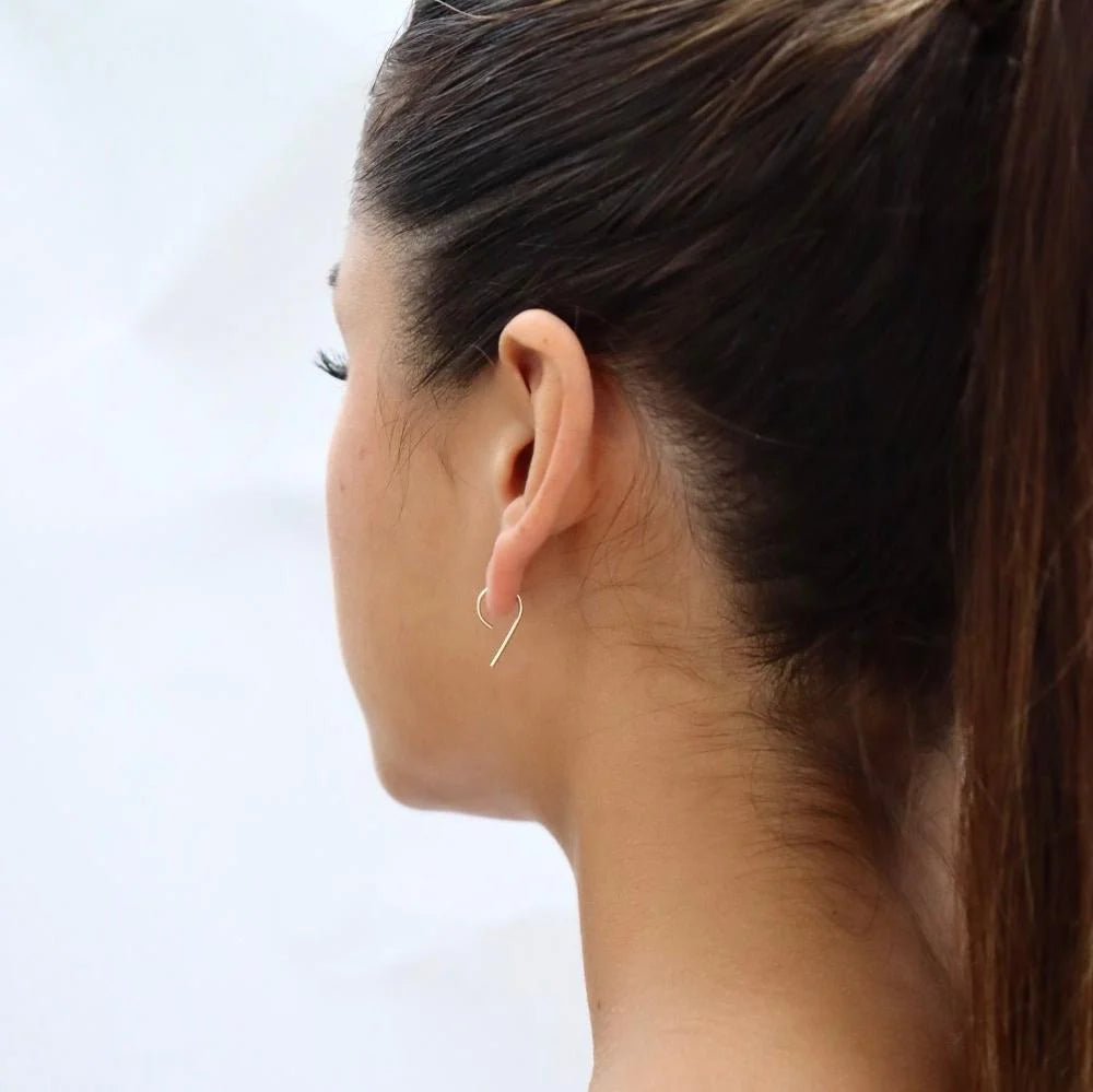 Model with dark hair in a high ponytail wearing Token Jewelry The Nines earrings in gold.