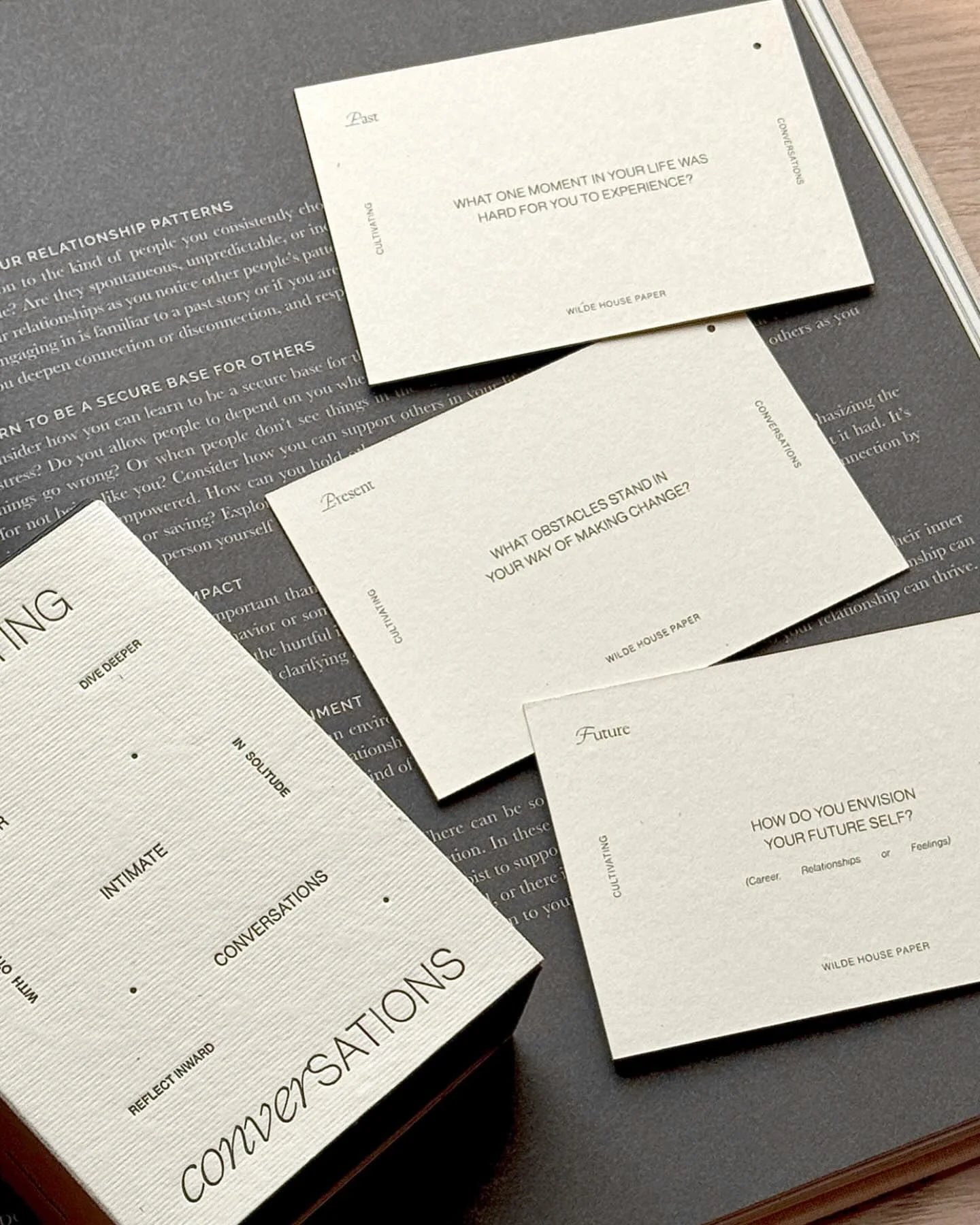 Several Wilde House Paper Cultivating Conversations cards spread out on a book with thoughtful prompts visible.