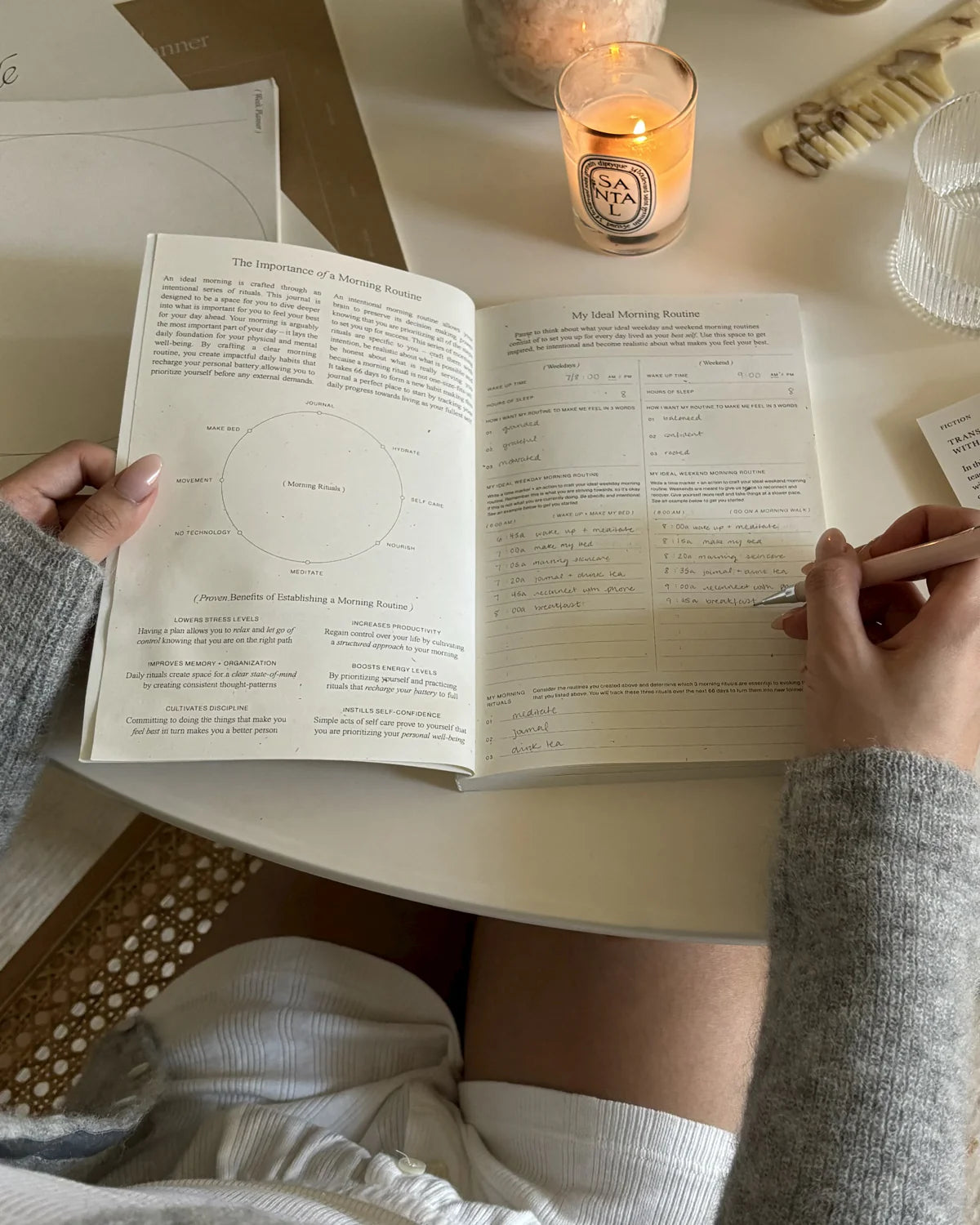 Person filling out the Wilde House Paper Morning Routine Journal ideal routine section with a santal candle beside.