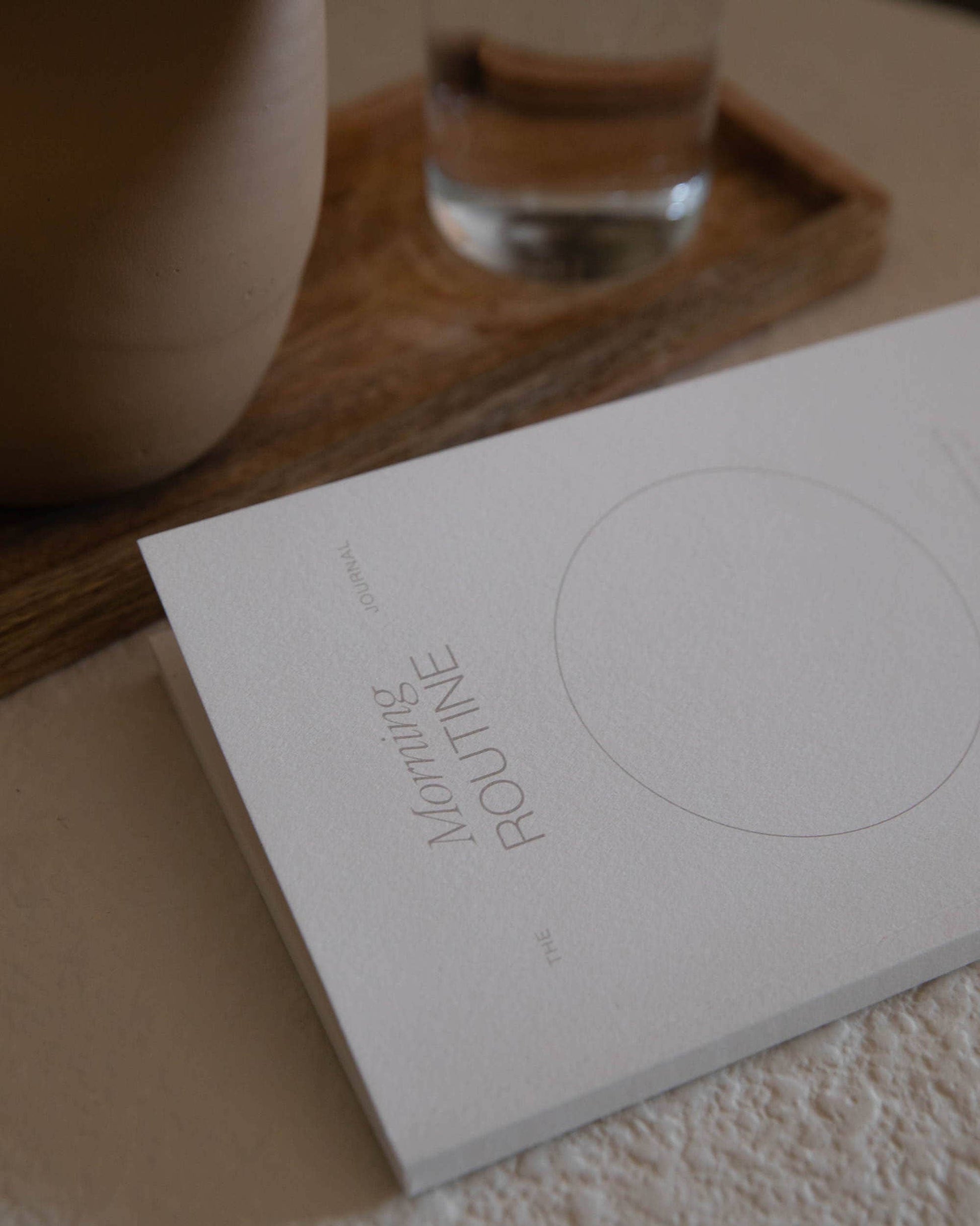 Wilde House Paper Morning Routine Journal placed on a wooden tray next to a glass of water.