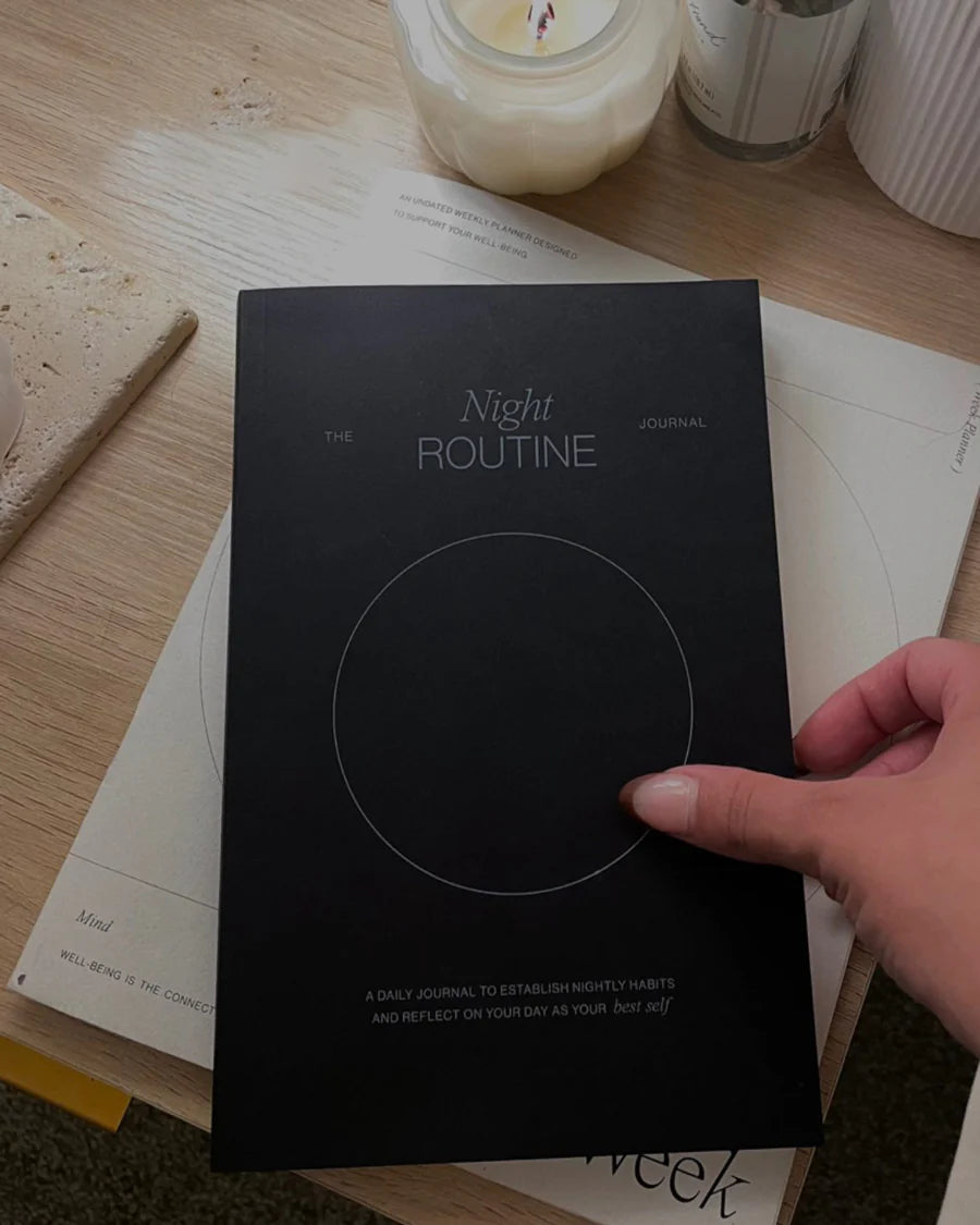 Hand holding the Wilde House Paper Night Routine Journal on a desk with candles.