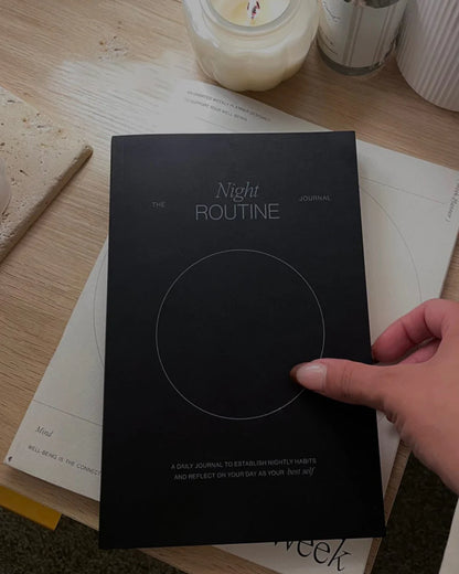 Hand holding the Wilde House Paper Night Routine Journal on a desk with candles.