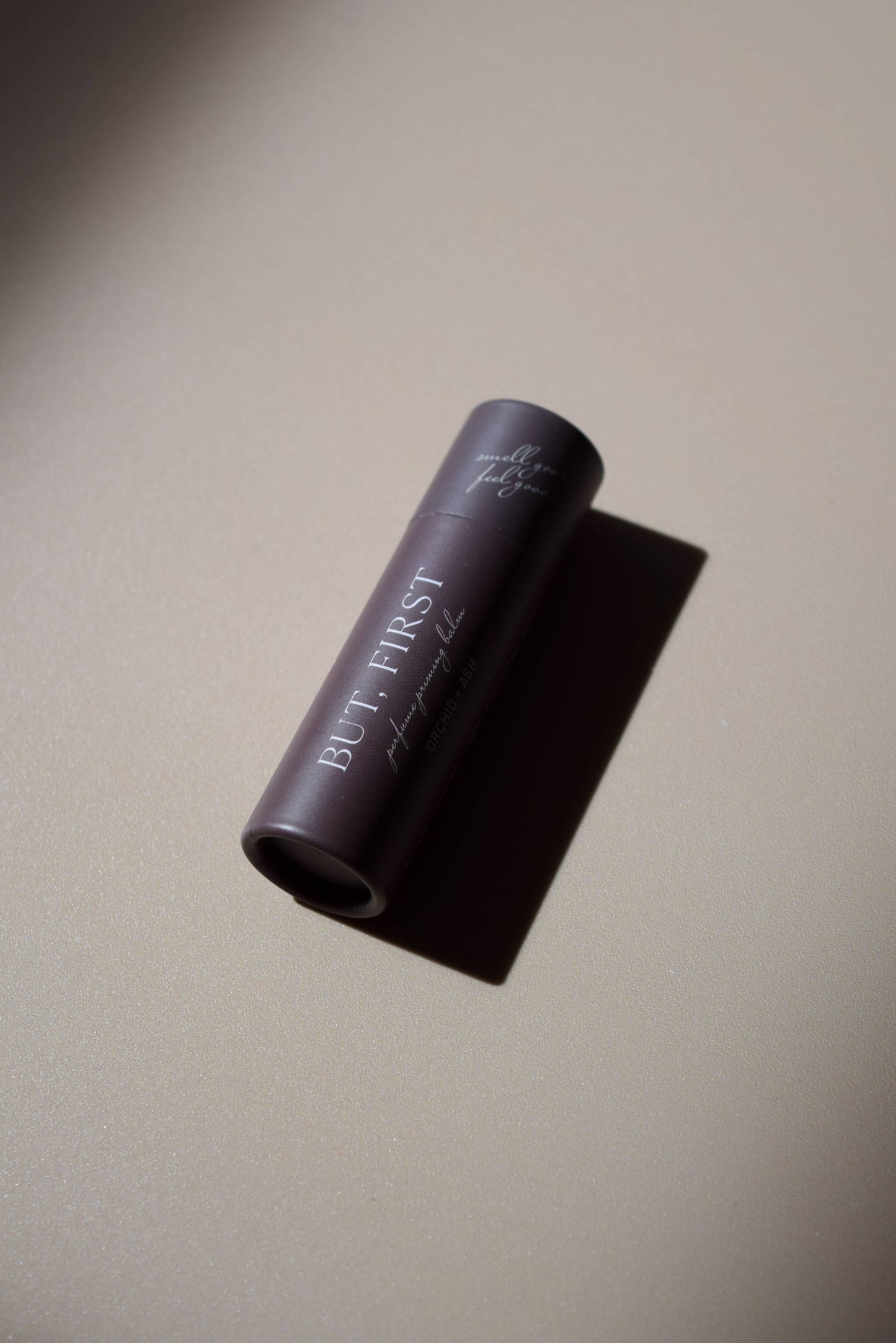But First natural perfume balm by Orchid & Ash laying flat, casting a dramatic shadow on a matte surface.